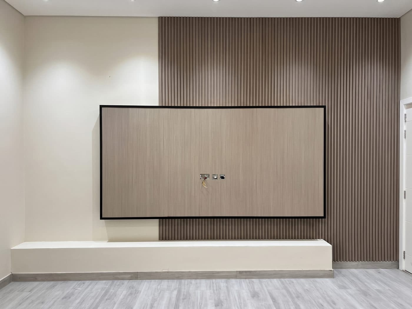 A slatted timber media wall with concealed lighting behind the fins.