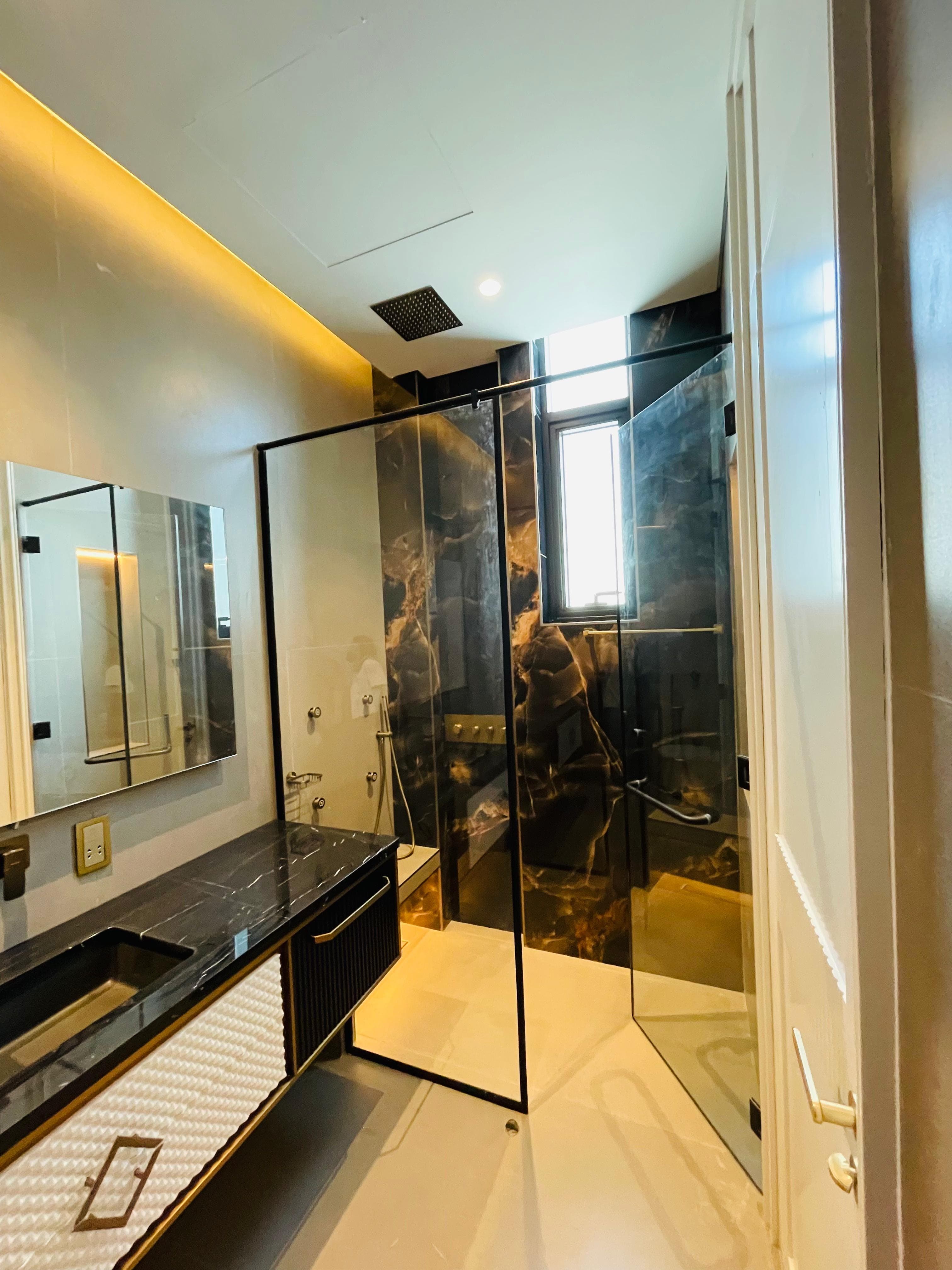 A bathroom in book-matched black marble with a glass shower screen