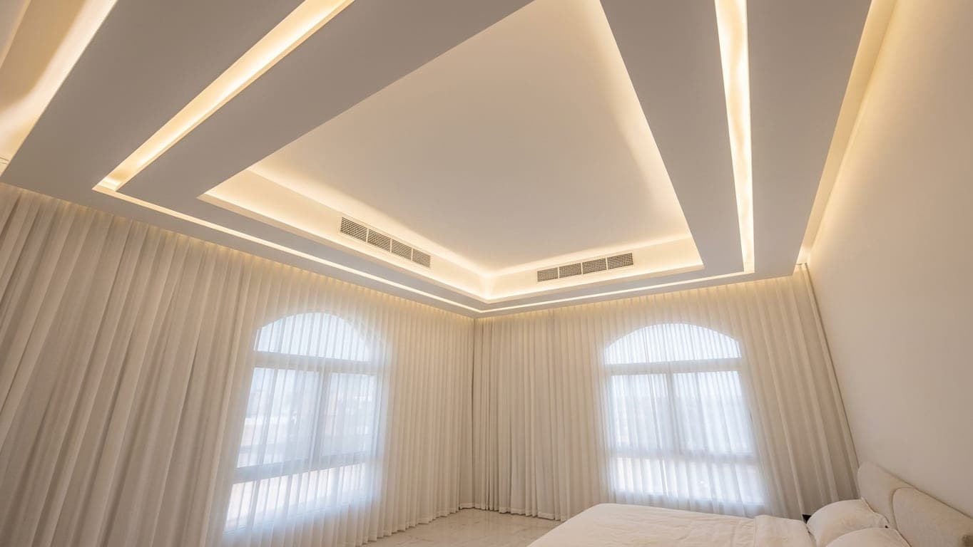 A bedroom framed by sheer drapery and a cove-lit ceiling