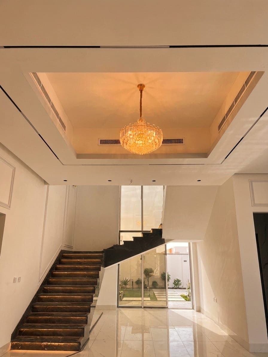 The stair hall, dark timber treads beneath a warm crystal chandelier
