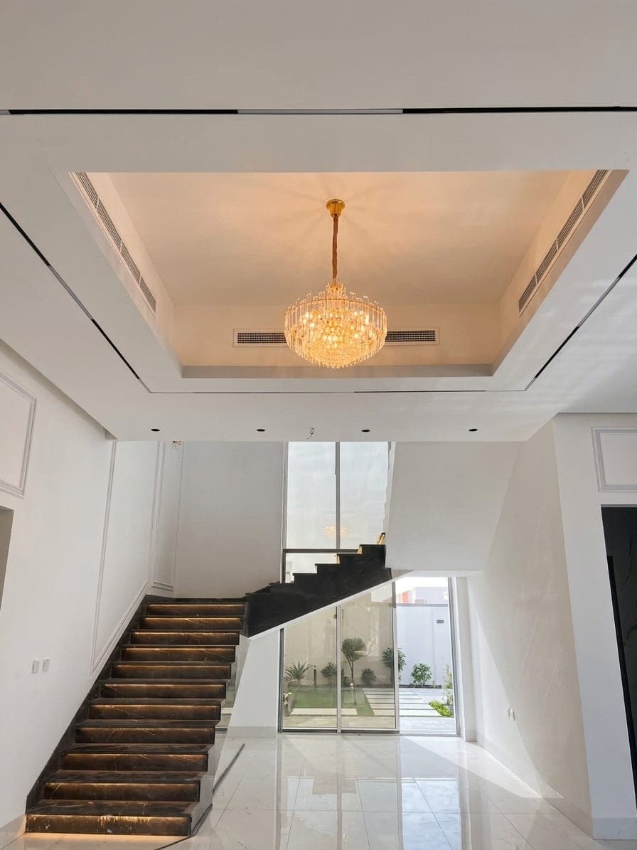The staircase rising through the reception under a cove-lit ceiling