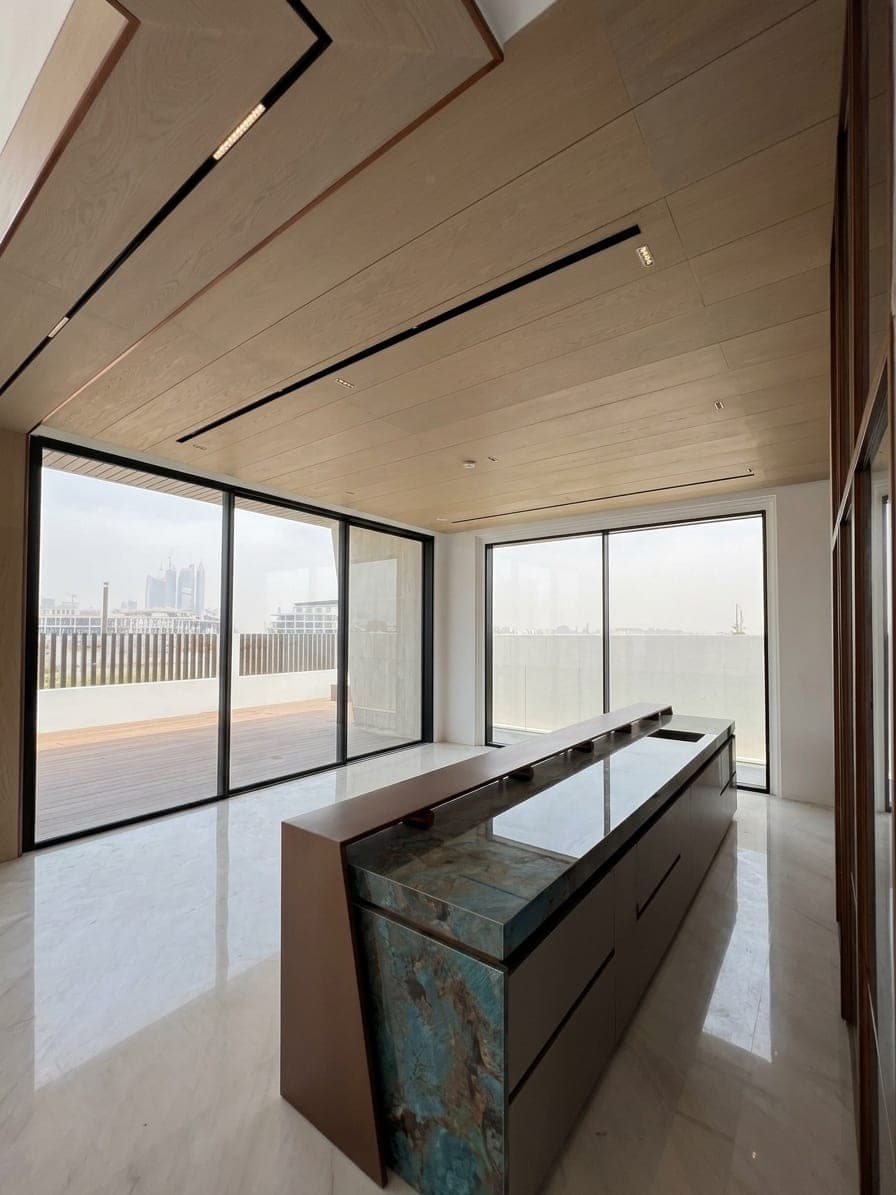 The kitchen — a blue-quartzite waterfall island under a timber-lined ceiling, open to the terrace