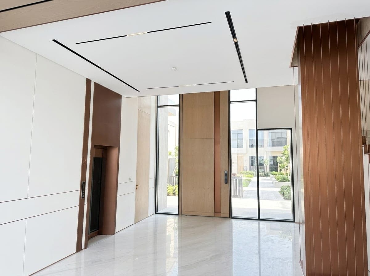 An interior lined in timber and marble, opening to the garden through full-height glass