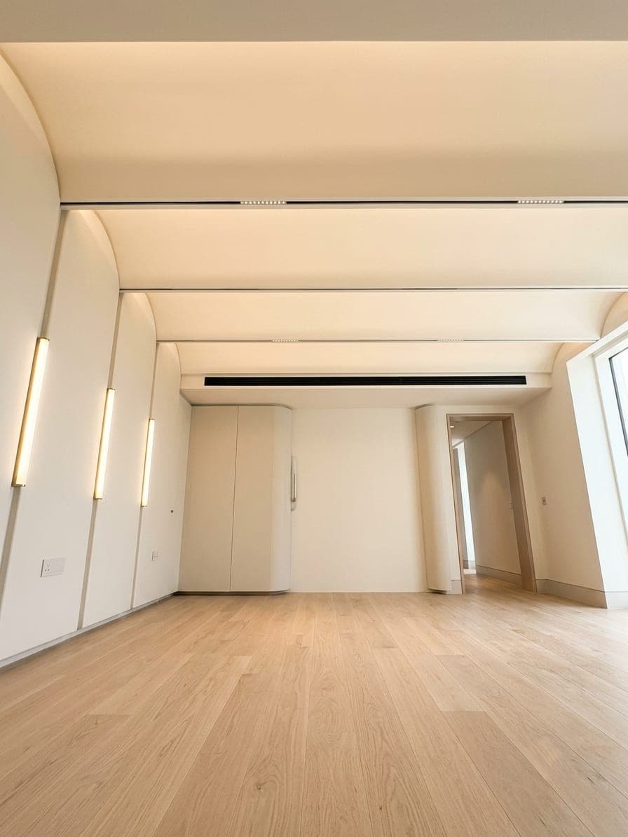 A curved-ceiling room with concealed linear wall lighting and oak floors